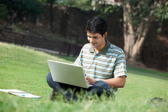 Student with a laptop sitting in a park