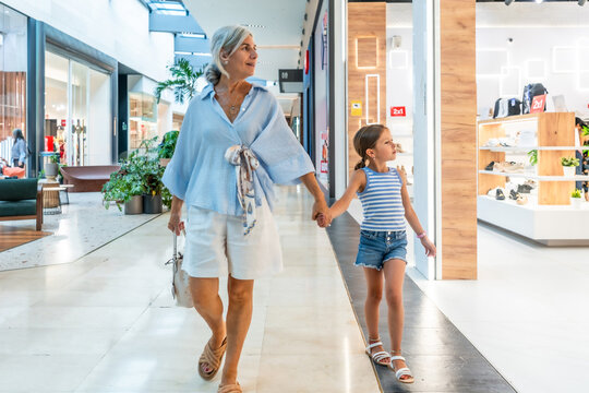 Grandmother holding granddaughter's hand walking in shopping mall