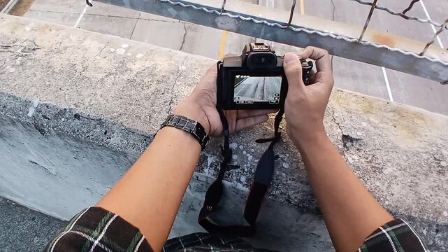 A man&rsquo;s point of view as he takes photos and videos, with his hand and camera visible against the backdrop of a highway