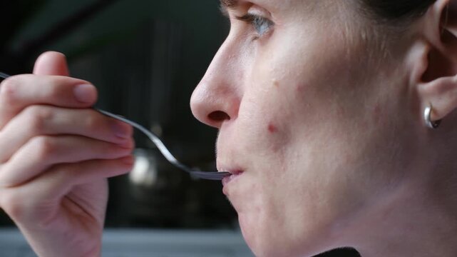 Close up profile of young woman face eats portion of beet salad from fork, putting food in her mouth and chewing, showcasing a daily mealtime routine in a kitchen. Woman eating beet salad with fork