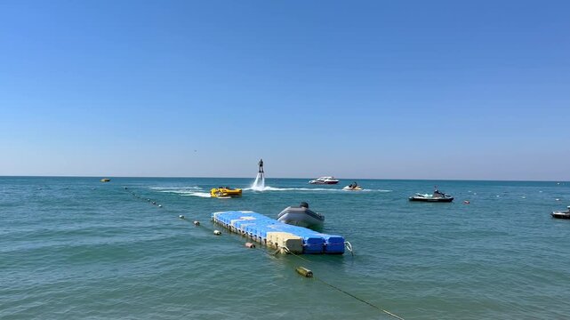 Turkey. 21.07.2026 Man flying on flyboard above sea water. Athlete performing extreme water sport activity near floating pier and boat on sunny day at seaside summer resort vacation.