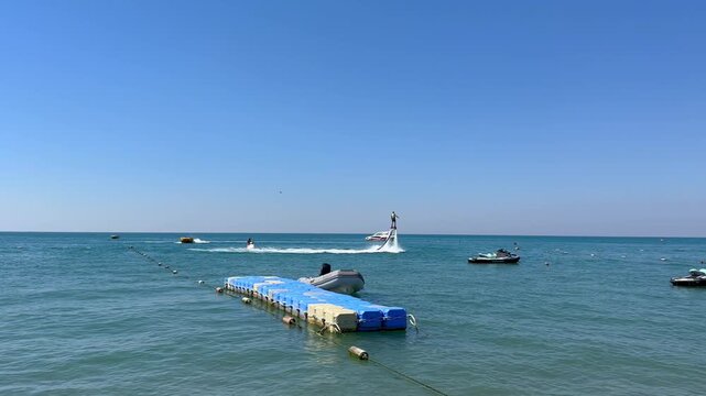 Turkey. 21.07.2026 Man flying on flyboard over blue sea surface. Water sport athlete hovering in air above ocean waves. Summer vacation activity near floating dock in sunny weather.