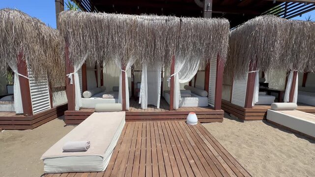 Turkey. 21.07.2026 Empty wooden beach cabana with white curtains on a sandy shore. Tropical sunbed setup with wooden deck for summer vacation. Resort relaxation area by the ocean.