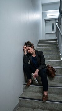 A woman sits dejectedly on a stairwell, head in hand, looking exhausted and defeated