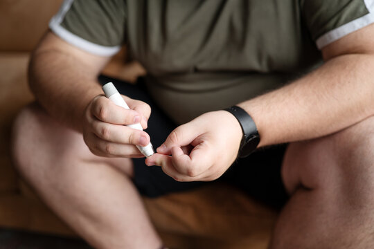 Man pricking finger with lancet pen to test blood glucose level at home, diabetes management concept.