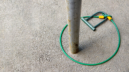 Green bicycle cable lock and u lock are seen joined together and wrapped around a metal pole on a textured asphalt ground. Symbolizing irony. Lack of true security © Newleks