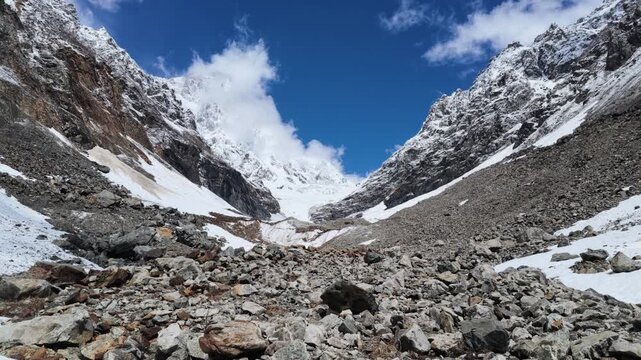 Snow capped mountain peaks at Chalaadi glacier in Svaneti Georgia with rocky glacier moraine foreground and dramatic blue sky, majestic alpine scenery