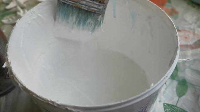 Paintbrush dipping bucket pristine white paint preparing for home improvement.