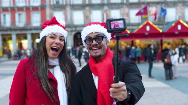 Happy young couple in santa hats vlogging for social media at a christmas market in madrid