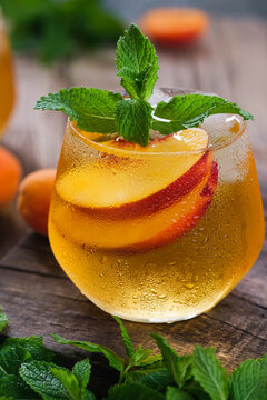 Cold summer beverage with sliced fresh nectarines, mint leaves, and ice in a condensed glass, garnished with fresh mint and fruit on a textured tabletop.
