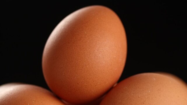 Pile of raw brown chicken eggs slowly rotating on a black background.