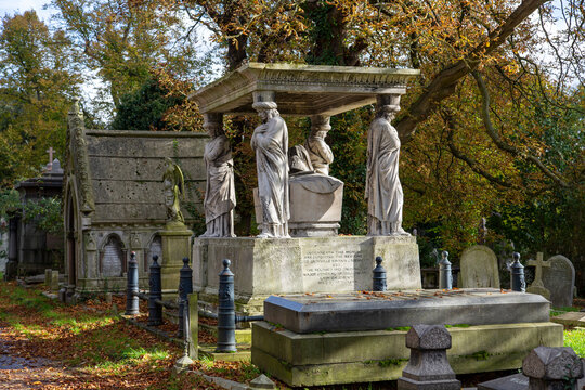 Caryatids on a Victorian stone memorial among autumnal trees and gravestones in Kensal Green Cemetery, one of London's Magnificent Seven, west London, UK