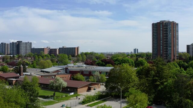 Slow aerial drone establishing shot overlooking a suburban residential neighborhood featuring high-rise apartment buildings, detached family homes, community buildings, mature green trees, and lush sp