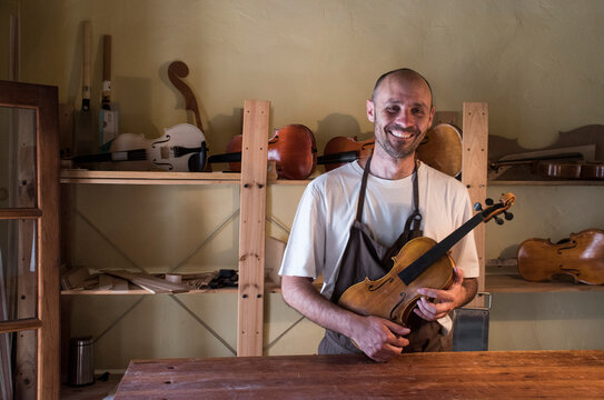 Smiling luthier holding a violin in his workshop