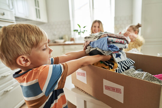 Boy arranging clothes in donation box with family in background
