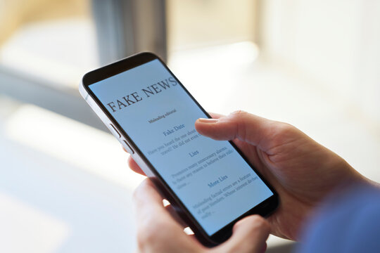 Hand holding smartphone displaying fake news article