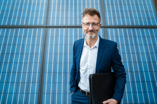 Portrait of smiling businessman holding folder standing in front of solar panels