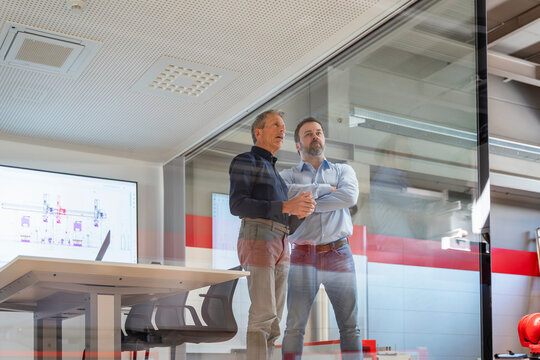 A manager and an engineer look through a glass window at the office