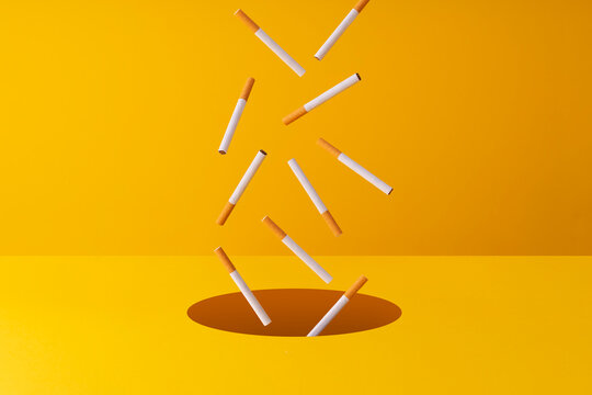 Cigarettes falling into a hole in yellow background