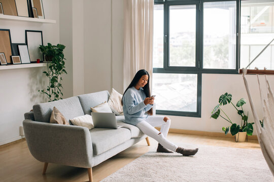 Young woman sitting on couch at home looking at smartphone