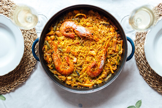 Pan of ready-to-eat paella with shrimps and two glasses of white wine