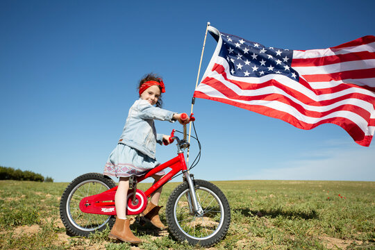 Girl with bicycle and American flag on field in remote landscape
