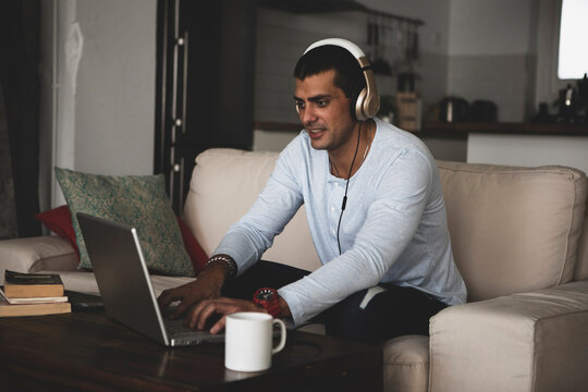 Young man sitting on sofa at home wearing headphones and using laptop