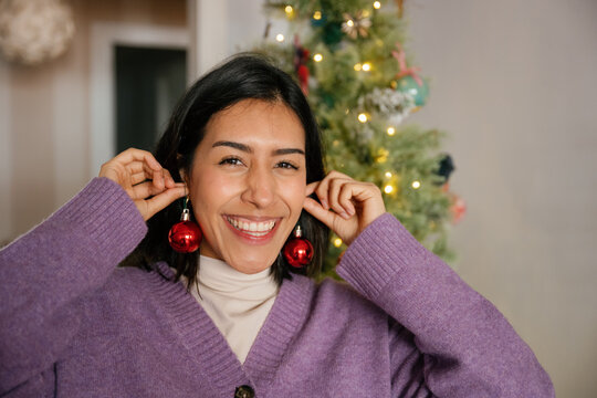 Smiling woman holds red baubles as earrings at home