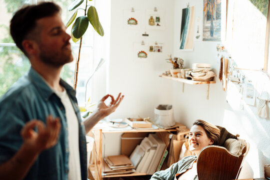 Smiling woman looking at man meditating at home