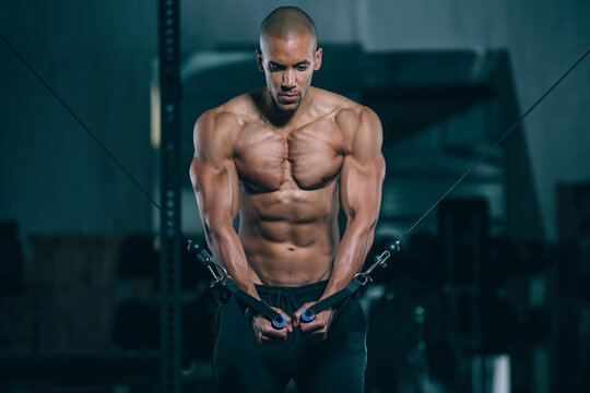Young man training pectoral muscles at cable crossover in gym