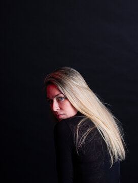 Serious blonde woman looking over shoulder on black background