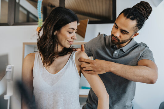 Physiotherapist examining shoulder of female patient in practice