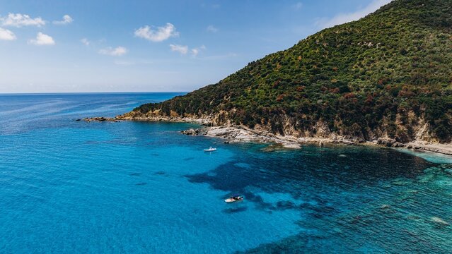 Small boats float on turquoise water near a rocky coast in Sardinia