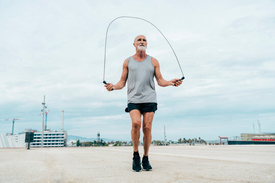 Fit retired senior man exercising with jump rope on footpath