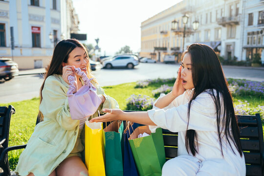 Surprised woman looking at friend holding purse on bench