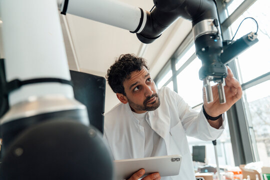 Scientist examining robotic arm with tablet in modern laboratory