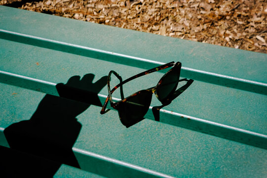 A shadow falls beside sunglasses on a green outdoor bench