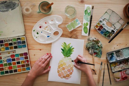 Woman's hand painting aquarelle of a pineapple on desk in her studio