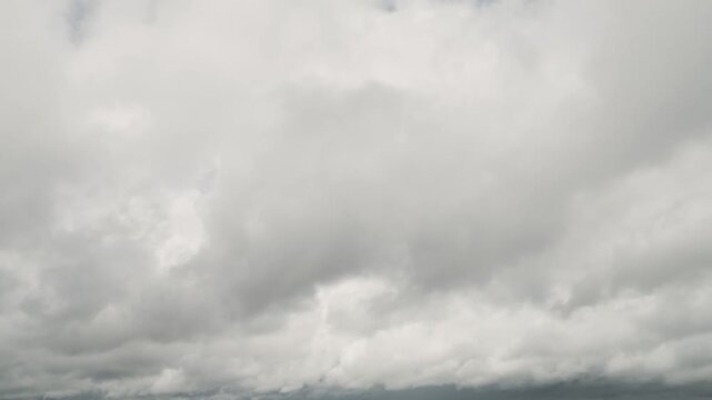 Low-angle view looking up at thick, overcast clouds moving across the gray sky timelapse during a overcast day.