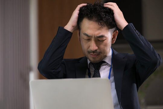 残業でパソコンのトラブルや仕事の問題に悩み頭を抱える日本人ビジネスマン