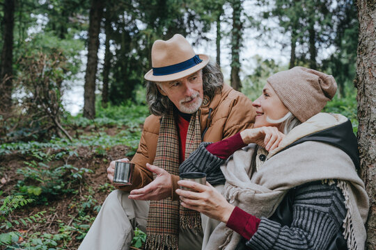 Woman with senior man having tea sitting in forest