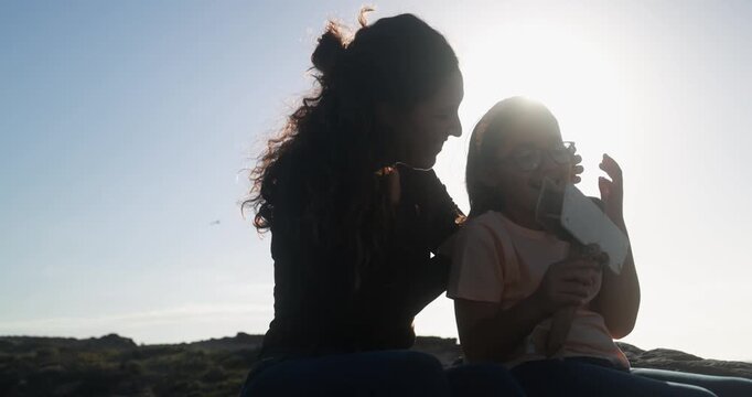 Happy latin mother having playful time with daughter using wood airplane during sunset outdoor - Holiday, summer and family lifestyle concept