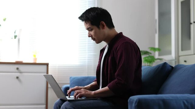 Young asian man working from home on a laptop and getting progressively more tired.