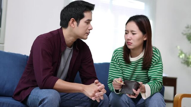 Young couple arguing about financial problems, showing empty wallet and unpaid bills on the table.