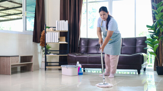 Professional female cleaner mopping a bright modern living room with a mop and bucket, representing house cleaning, housekeeping, home maintenance, hygiene, sanitation, domestic service, 
