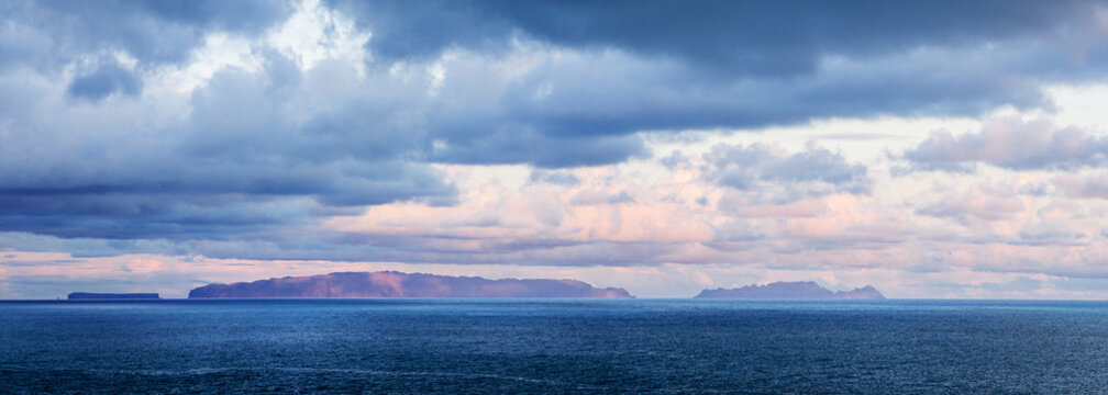 Wide panoramic view of the distant Desertas Islands silhouette on the ocean horizon under sunset clouds from Canico coast, Madeira, Portugal.