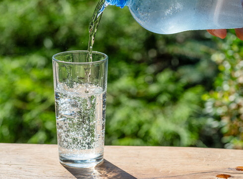 Pouring fresh water from plastic bottle into clear glass outdoors