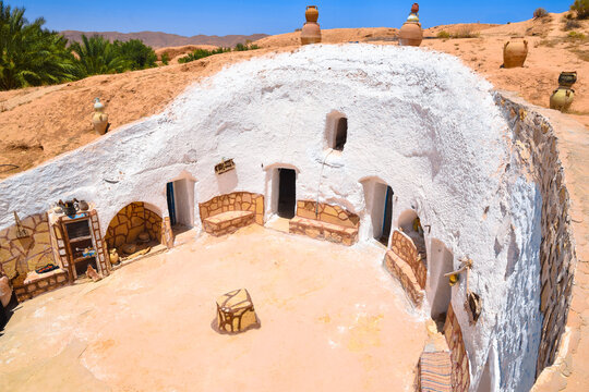 Courtyard of a traditional berber cave house with white walls, blue wooden door and orange stone bench in Sidi Meta near Matmata, Tunisia.