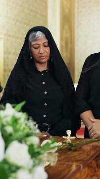Sad, people and flower at funeral with coffin, condolences and memorial service for deceased. Family, widow or rose on casket at church for remembrance, final goodbye and burial for farewell ceremony