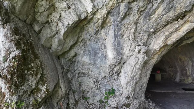 Ingresso di una grotta naturale con pareti rocciose stratificate, crepe irregolari e vegetazione spontanea alla base. Ambiente rupestre, ombroso e incontaminato